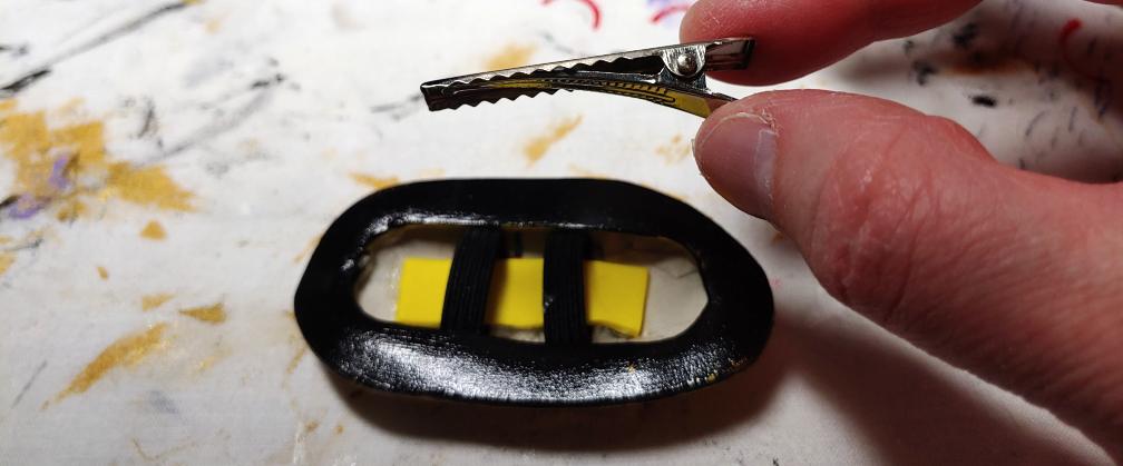 Holding a small alligator clip over the upside down hair clip on the table