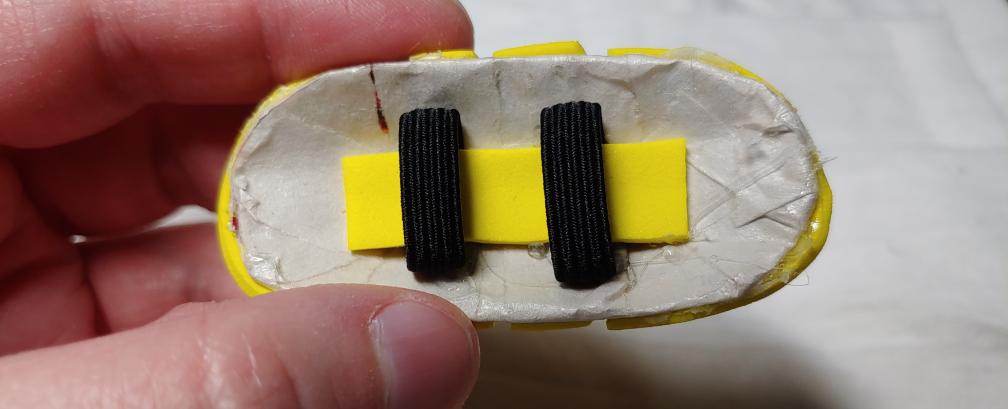 Yellow strip of foam inserted into the black elastic loops and glued down to the off-white paper mache