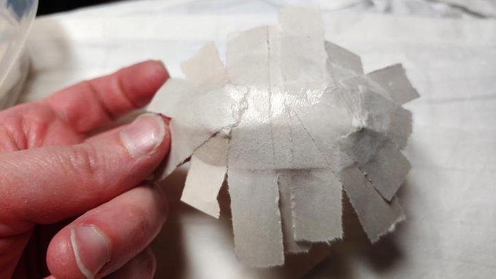 Top of a hair clip base covered in strips of paper. The paper is hanging over the edge