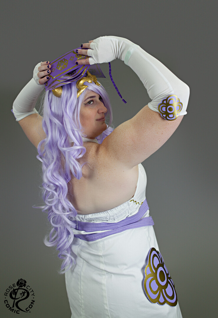 Over the shoulder, showing off the back of the cosplay with the ofuda held overhead.