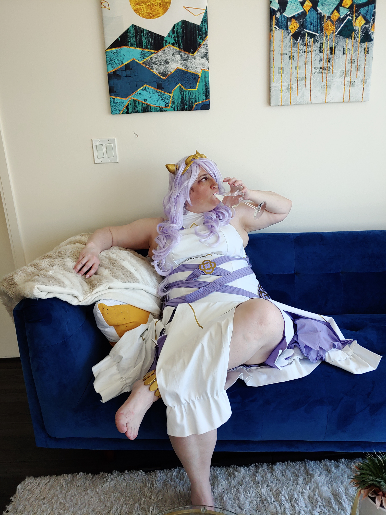 Camilla sipping wine on a blue sofa with blue and green artwork on the wall