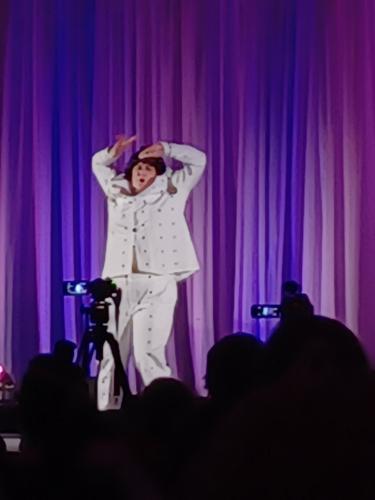 Bruno striking a JoJo pose on stage, hands over head with a purple and blue background
