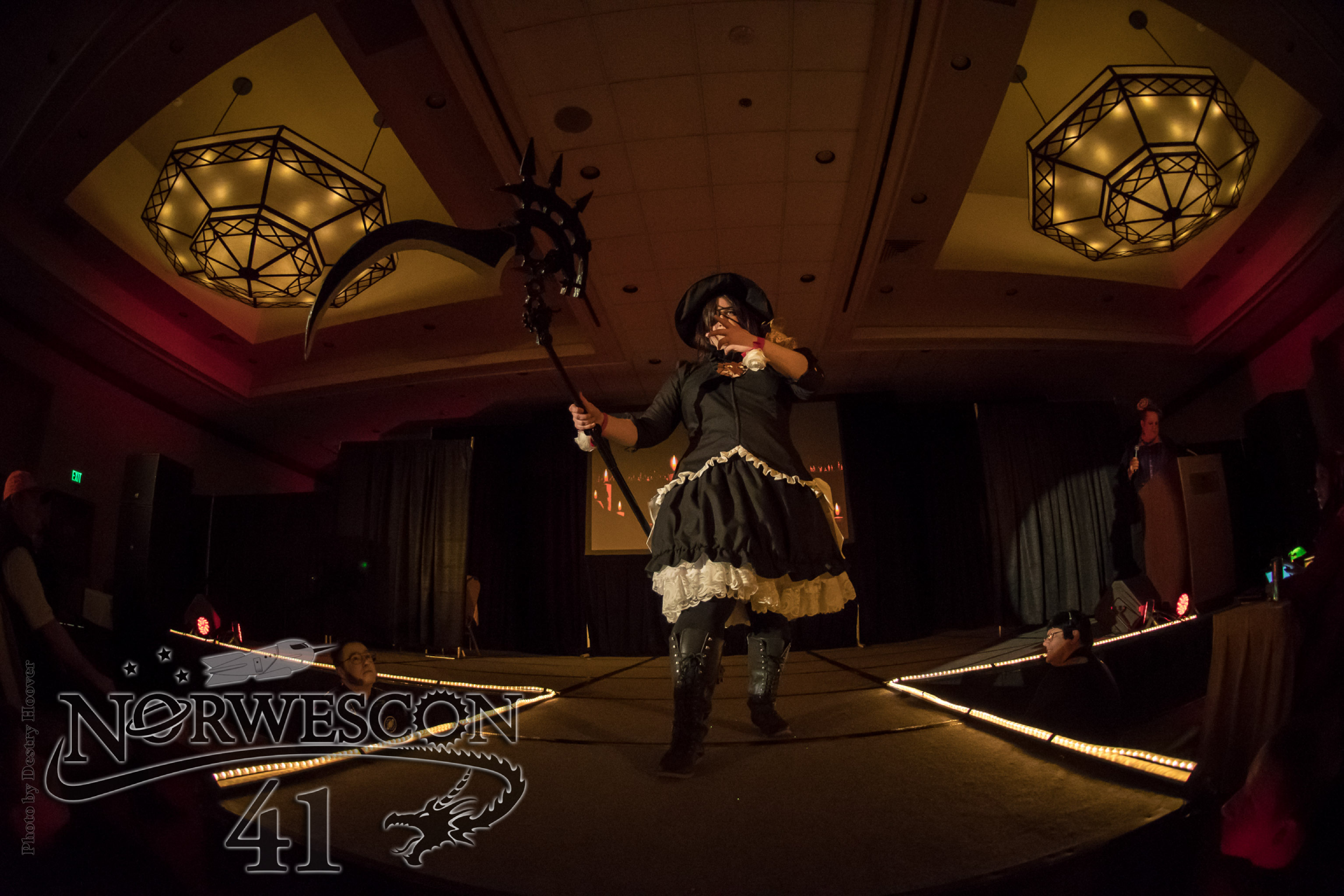 Edda walking on a catwalk, scythe extended left. Taken with a fisheye lens to show the ceiling and the stage
