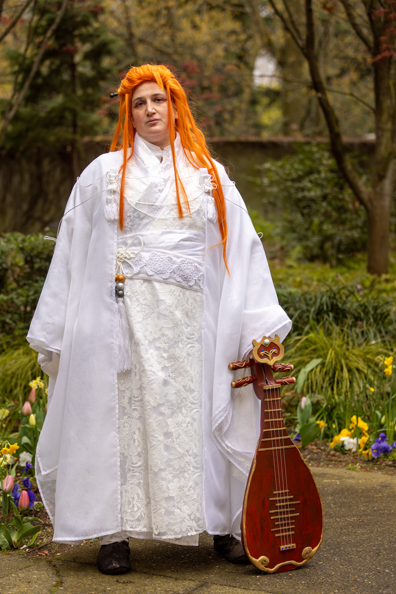 Standing, facing forward, pipa sitting bottom to the ground and resting in hand.