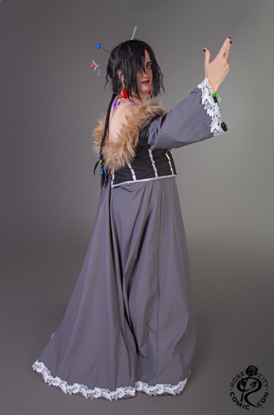 Lulu turned sideways with hand extended, showing off the back and train of the outfit