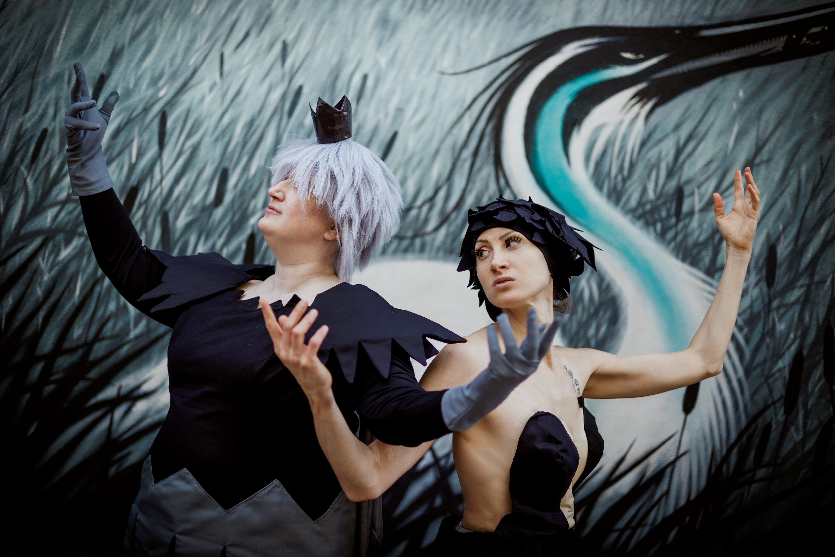 Kraehe and Mytho standing shoulder to shoulder, arms interwoven, in front of a black, white, and blue crane mural