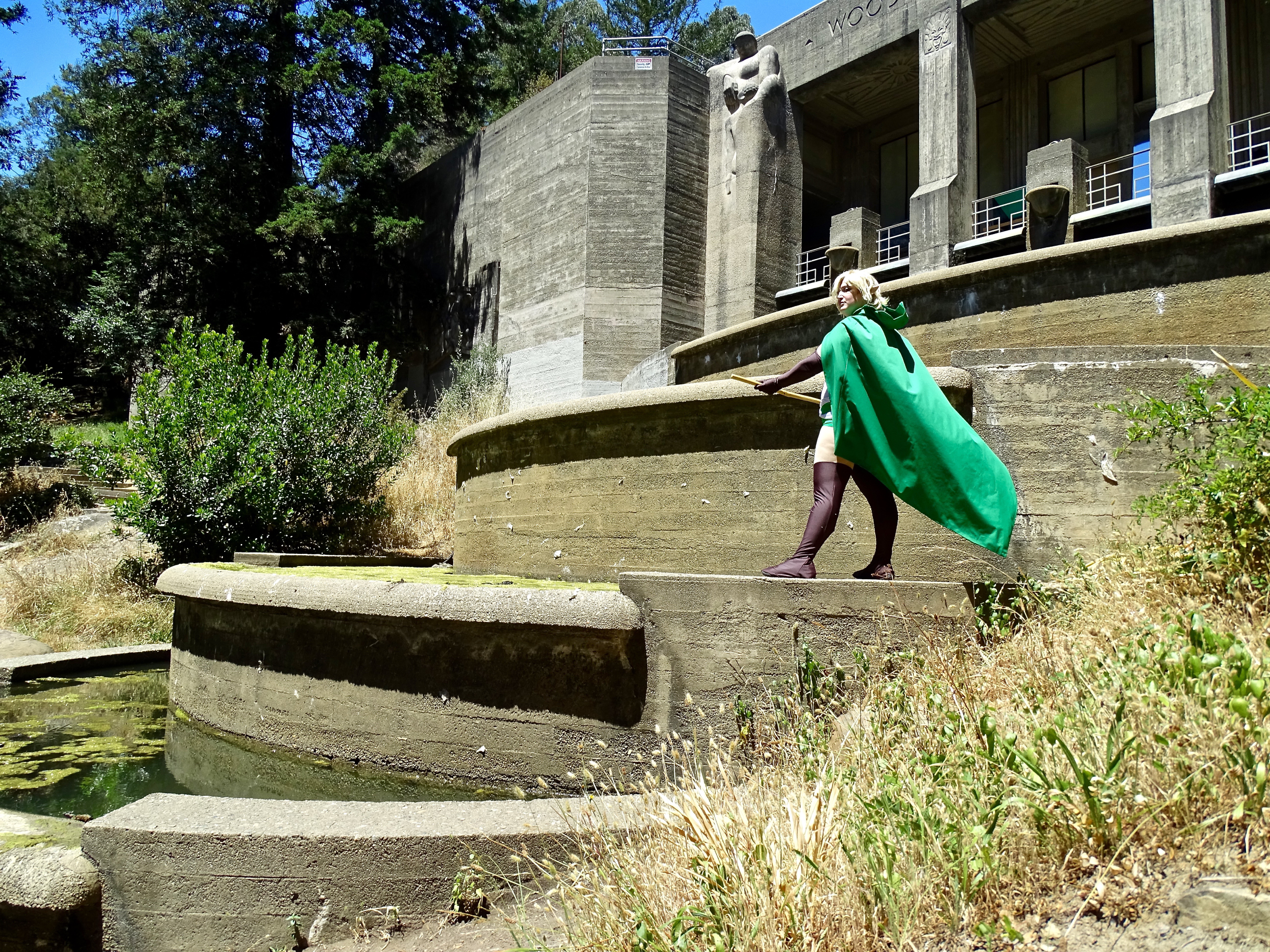 Ryu standing on the edge of a building fountain, green algae and lily pads floating in the nearby water
