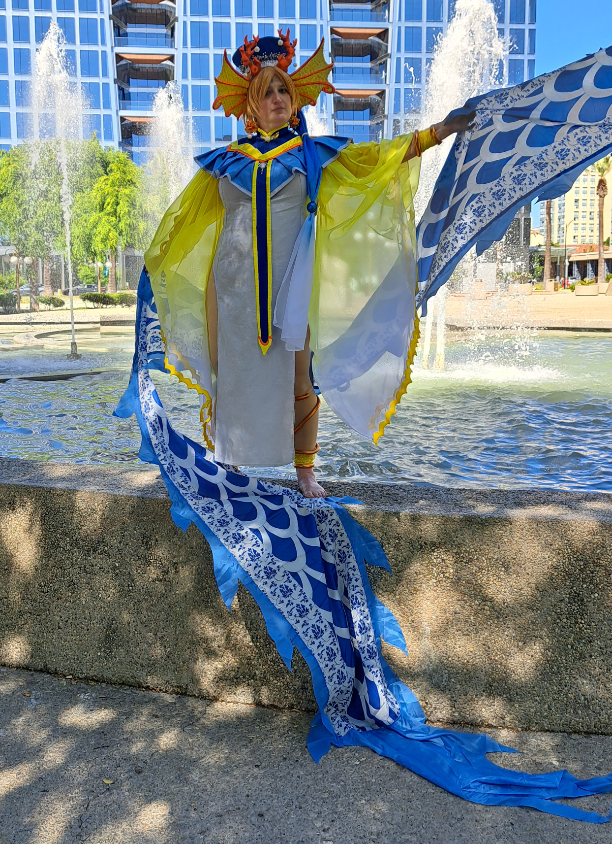 Yui holding a blue dragon streamer in front of a fountain