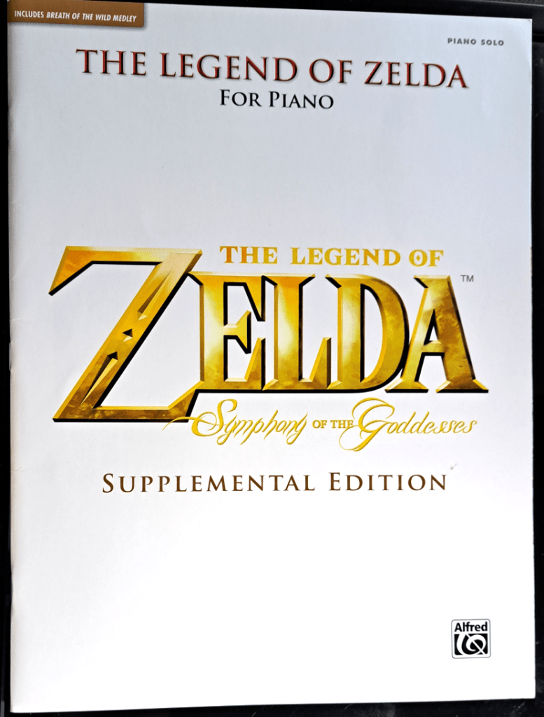 White front cover with "The Legend of Zelda Symphony of the Goddesses Supplemental Edition" written in gold