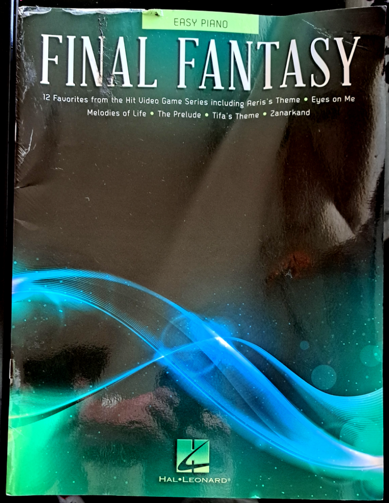 Front cover, mostly dark black reflecting the curtains and my hands with the camera. Blue and green streak across the bottom like the flow of aether and the Lifestream. The title at the top says "Easy Piano Final Fantasy" and lists all the songs out in small text underneath it.