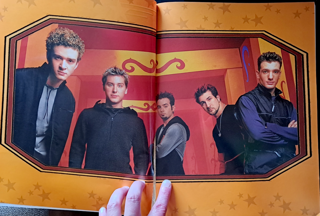 Color image of ★NSYNC with an orange border with stars. In the image from left to right, Justin, Lance, Chris, Joey, and JC. Behind them is a background of red and orange.