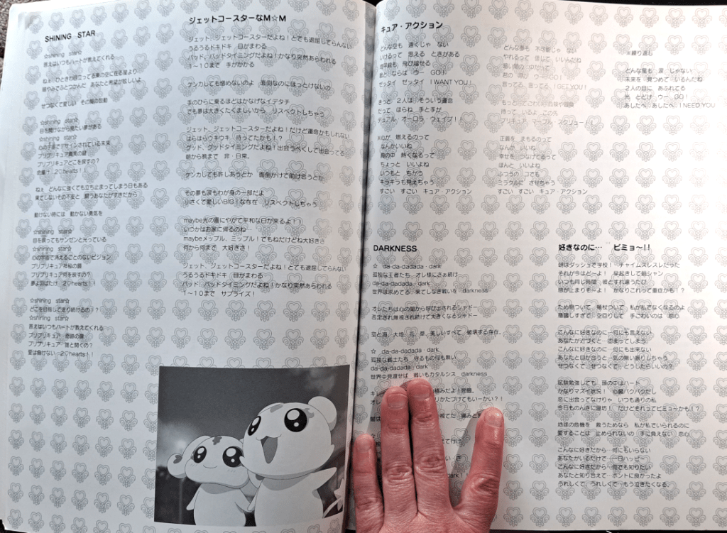 Lyrics page featuring several songs written in Japanese. The background is the PreCure heart symbol. At the bottom is a screenshot of Mepple and Mipple together.