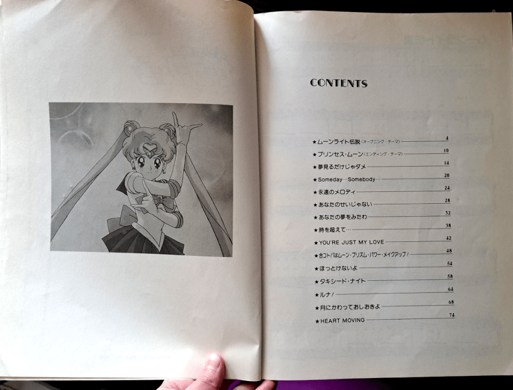 Two pages with the table of contents. Left page: grayscale image of Sailor Moon with her arms crossed from her intro speech
Right page: list of songs and the pages they appear on. For text, refer to Song List above.