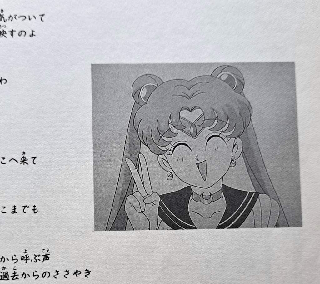 Gray screenshot of Sailor Moon smiling and giving a V sign with her hand