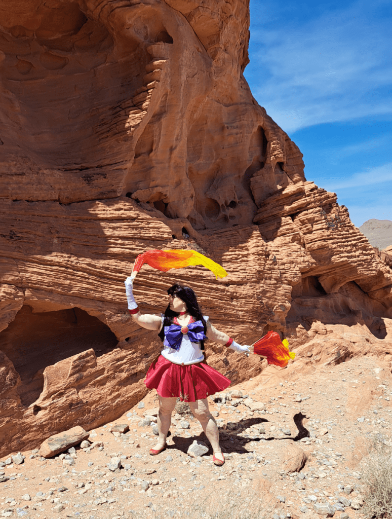 Mars in front of a tall layered rock with silk fire fans waving to the right