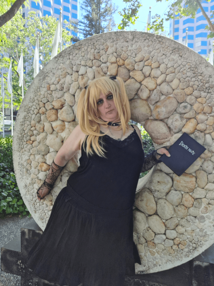 Misa standing against a round stone artwork, death note in hand, looking like she's been caught red-handed and is about to bolt