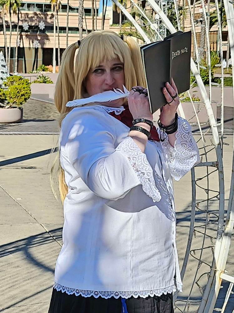 Misa turned sideways, holding the Death Note in one hand and a feather pen in the other